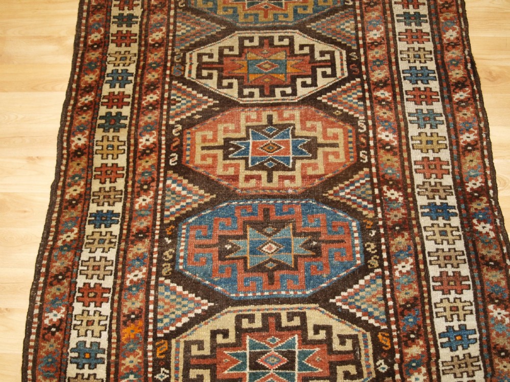 An antique hand-knotted Kurdish runner rug featuring a vertical sequence of octagonal Memling gul motifs in terracotta, blue, and cream shades. View V