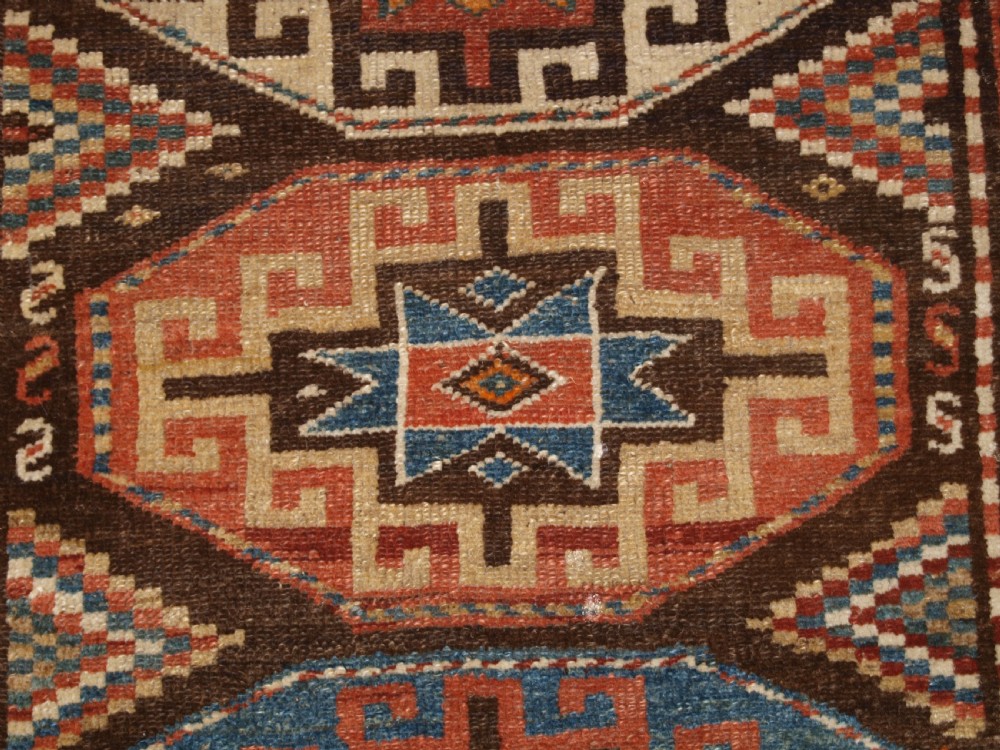 An antique hand-knotted Kurdish runner rug featuring a vertical sequence of octagonal Memling gul motifs in terracotta, blue, and cream shades. View VII