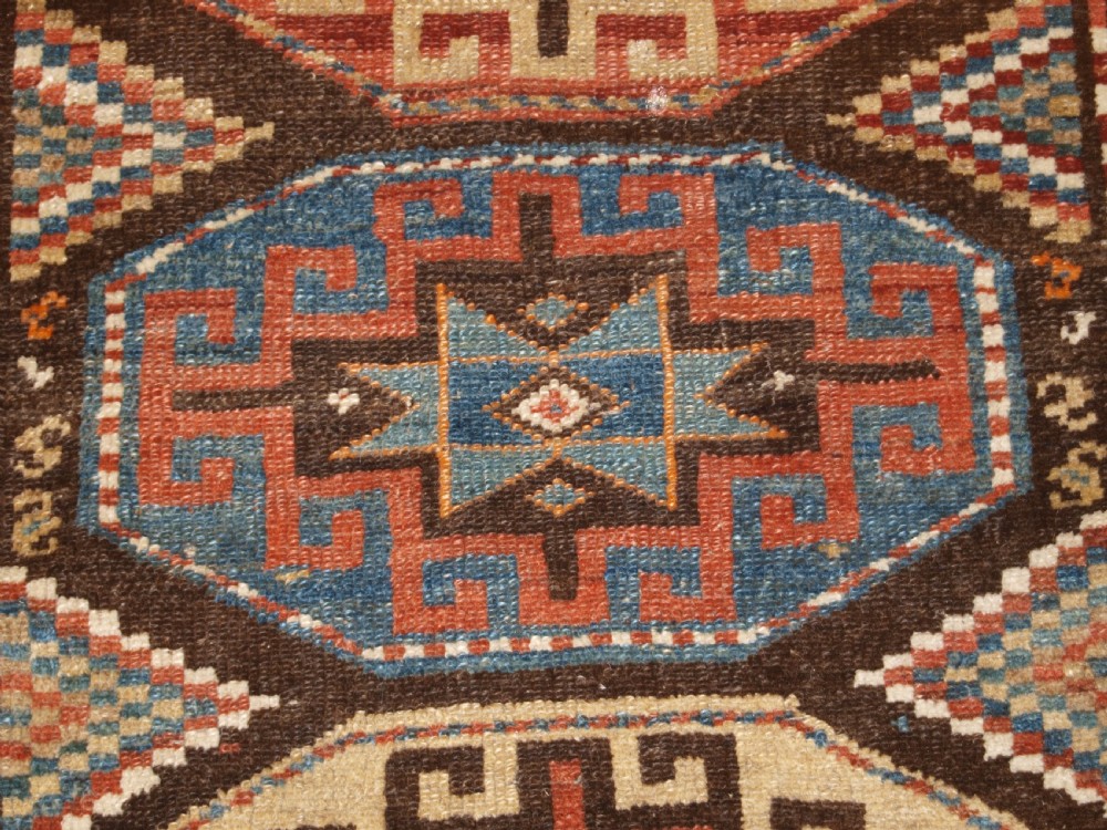 An antique hand-knotted Kurdish runner rug featuring a vertical sequence of octagonal Memling gul motifs in terracotta, blue, and cream shades. View X