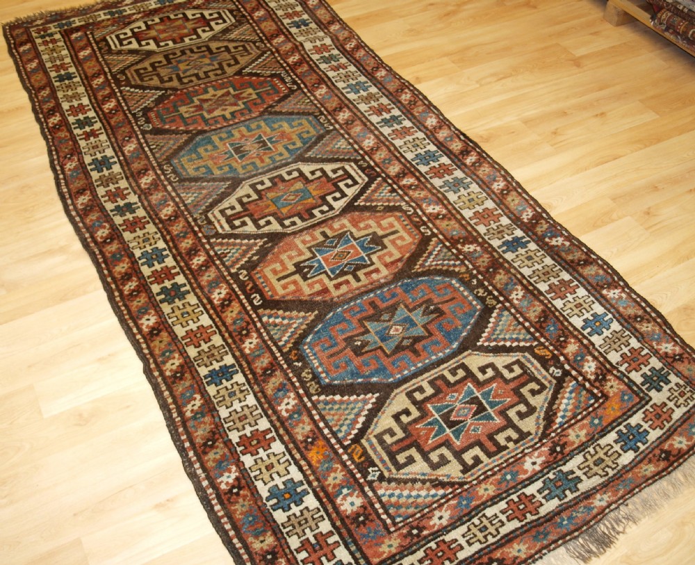 An antique hand-knotted Kurdish runner rug featuring a vertical sequence of octagonal Memling gul motifs in terracotta, blue, and cream shades. View XII