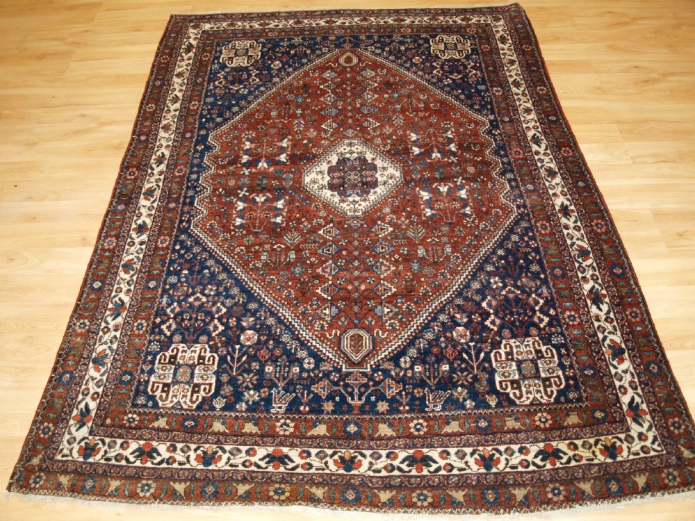 An antique hand-knotted Persian Abedeh rug featuring a central cream diamond medallion surrounded by a terracotta red field with navy blue corners.