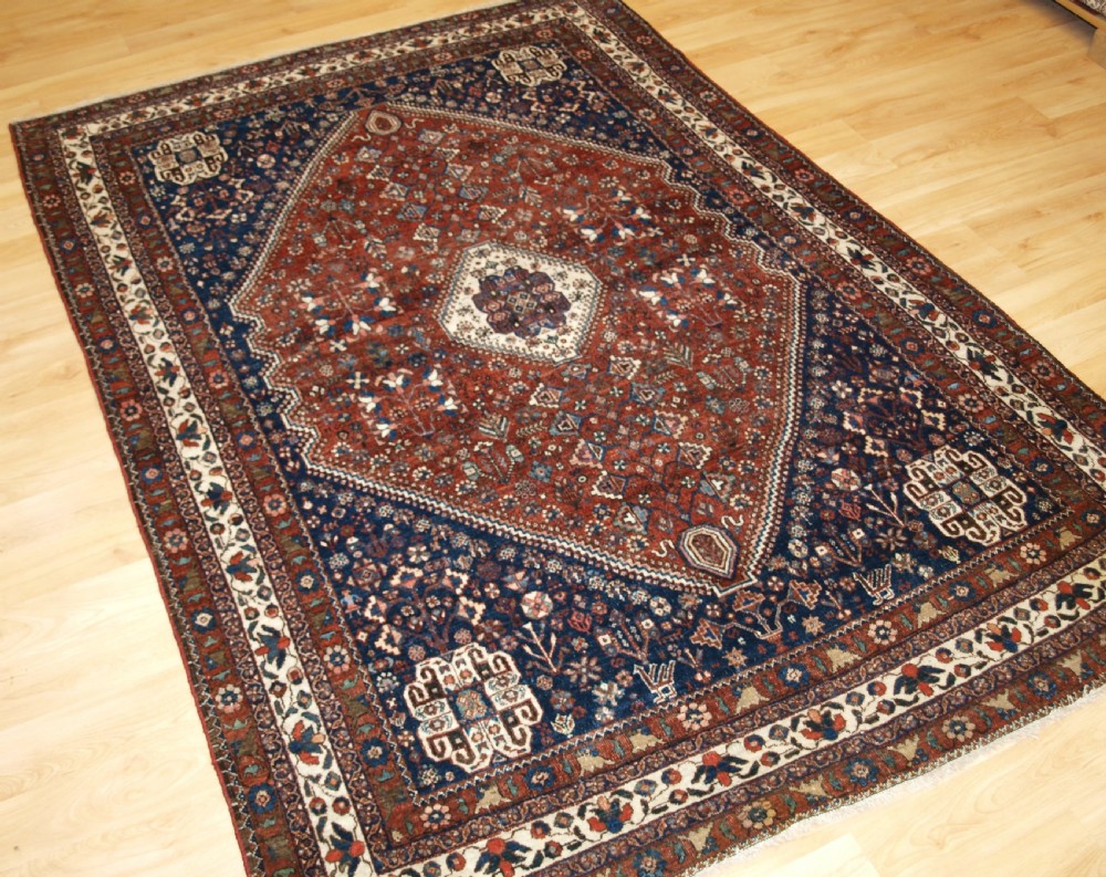 An antique hand-knotted Persian Abedeh rug featuring a central cream diamond medallion surrounded by a terracotta red field with navy blue corners. View III