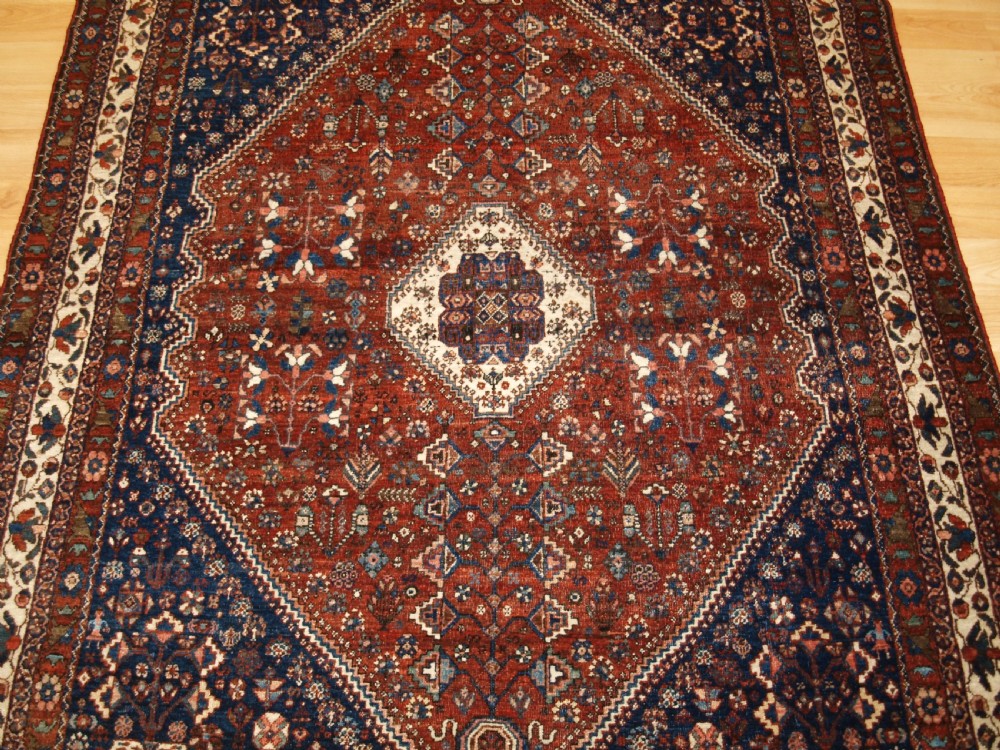 An antique hand-knotted Persian Abedeh rug featuring a central cream diamond medallion surrounded by a terracotta red field with navy blue corners. View V