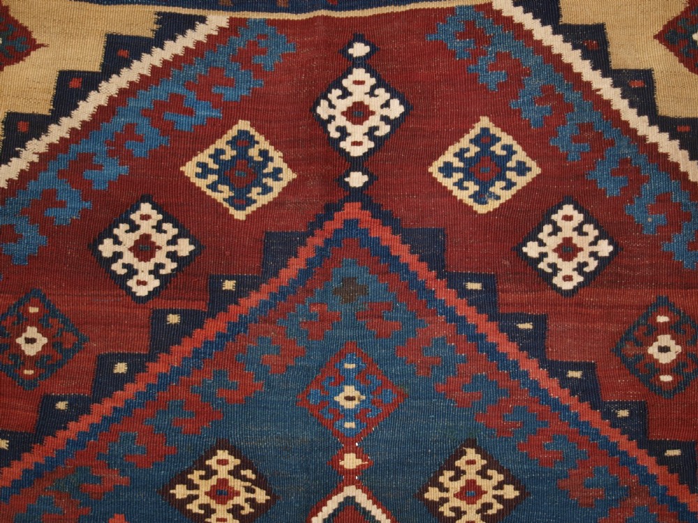 An antique Persian Qashqai flatweave wool kilim rug featuring two central blue and red diamond medallions framed by geometric tribal borders. View VII