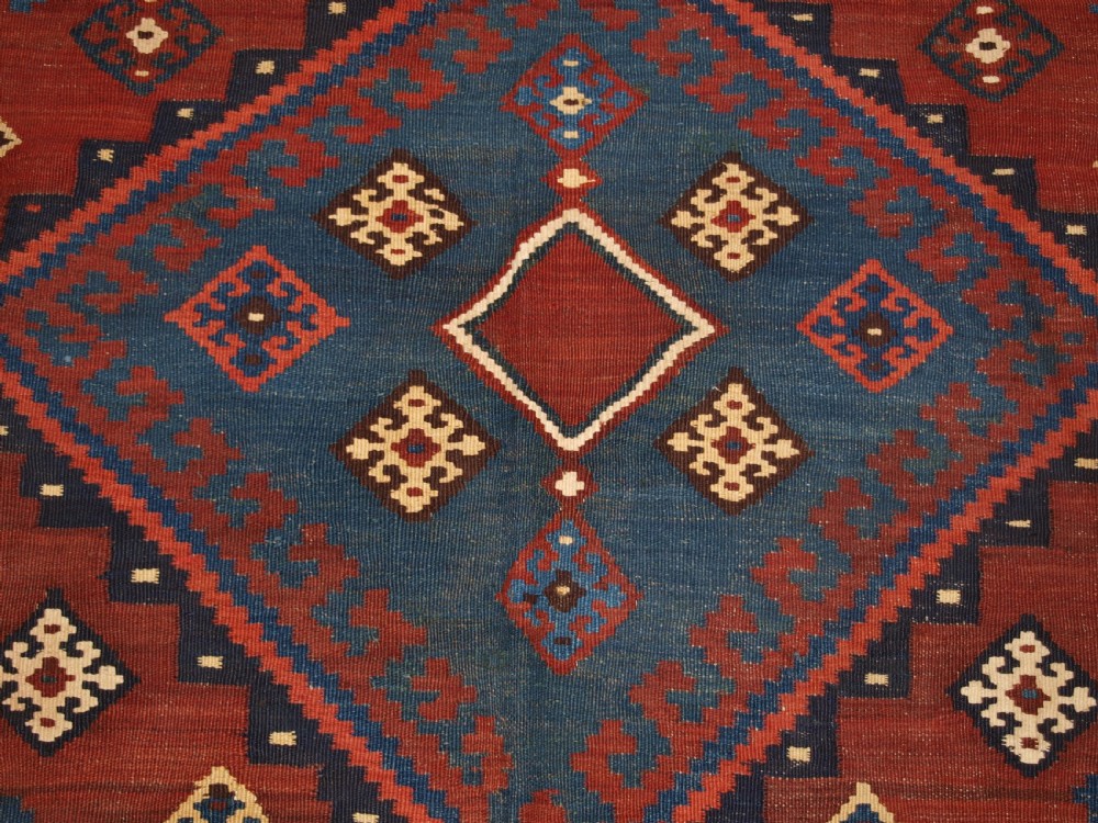 An antique Persian Qashqai flatweave wool kilim rug featuring two central blue and red diamond medallions framed by geometric tribal borders. View VIII