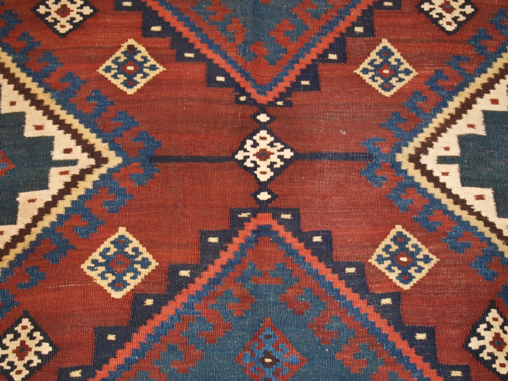 An antique Persian Qashqai flatweave wool kilim rug featuring two central blue and red diamond medallions framed by geometric tribal borders. View IX
