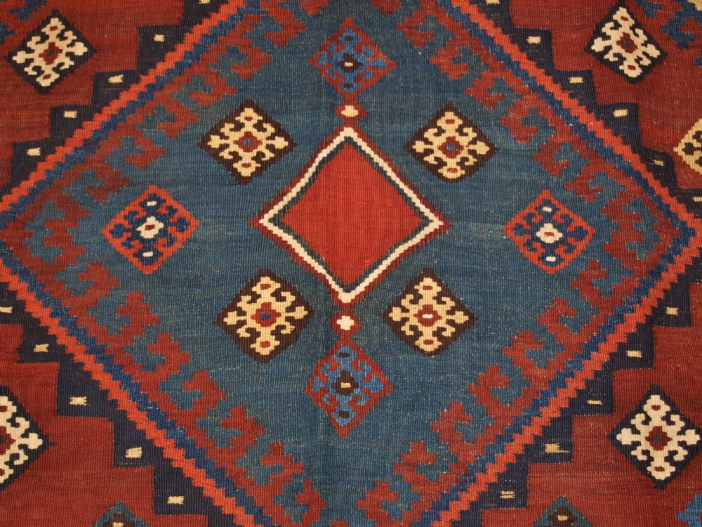 An antique Persian Qashqai flatweave wool kilim rug featuring two central blue and red diamond medallions framed by geometric tribal borders. View XI