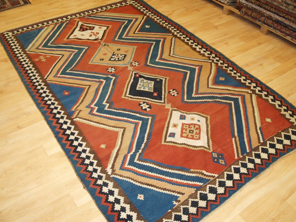 An antique flatweave Qashqai wool kilim rug featuring bold geometric diamond and chevron eye-dazzler patterns in terracotta red, indigo blue, cream, and brown. View II
