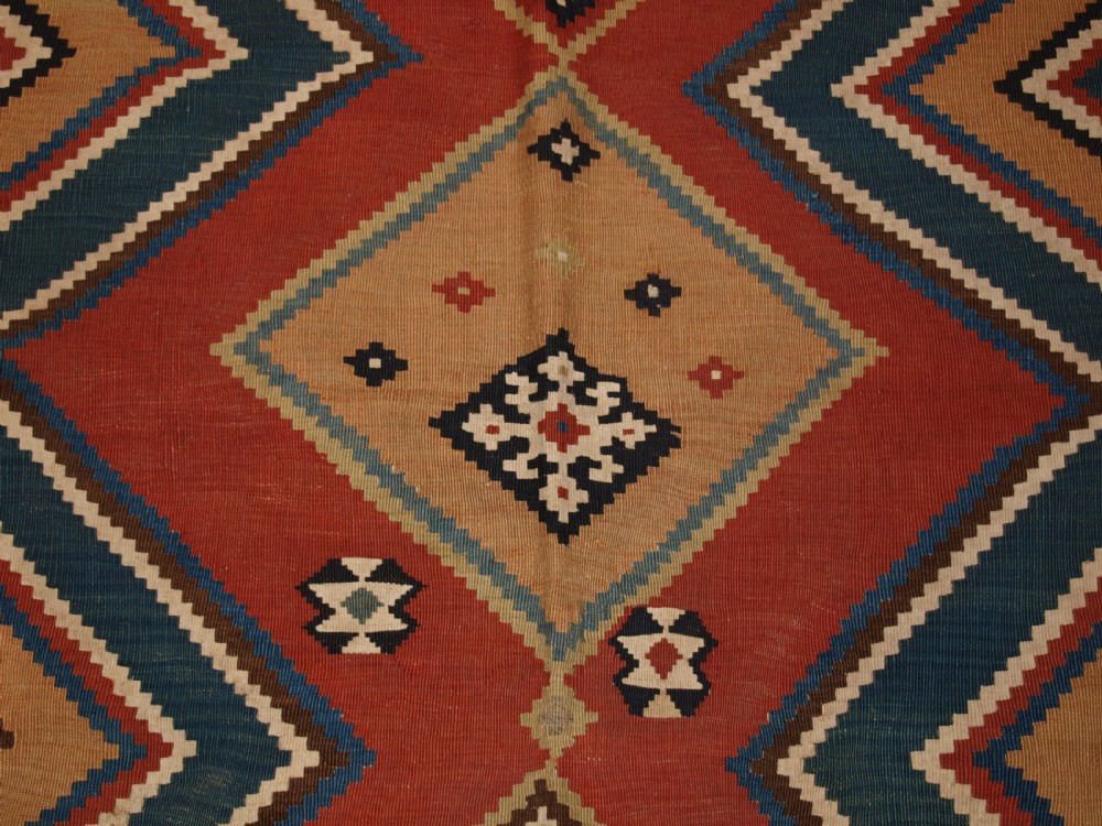 An antique flatweave Qashqai wool kilim rug featuring bold geometric diamond and chevron eye-dazzler patterns in terracotta red, indigo blue, cream, and brown. View VIII