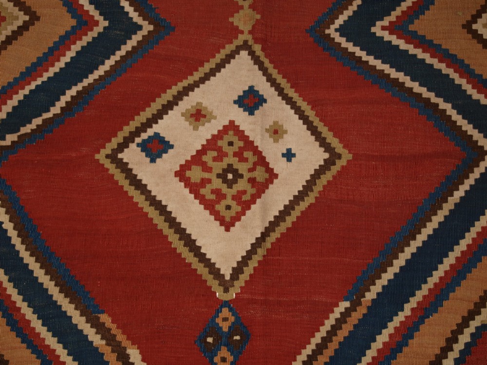 An antique flatweave Qashqai wool kilim rug featuring bold geometric diamond and chevron eye-dazzler patterns in terracotta red, indigo blue, cream, and brown. View IX
