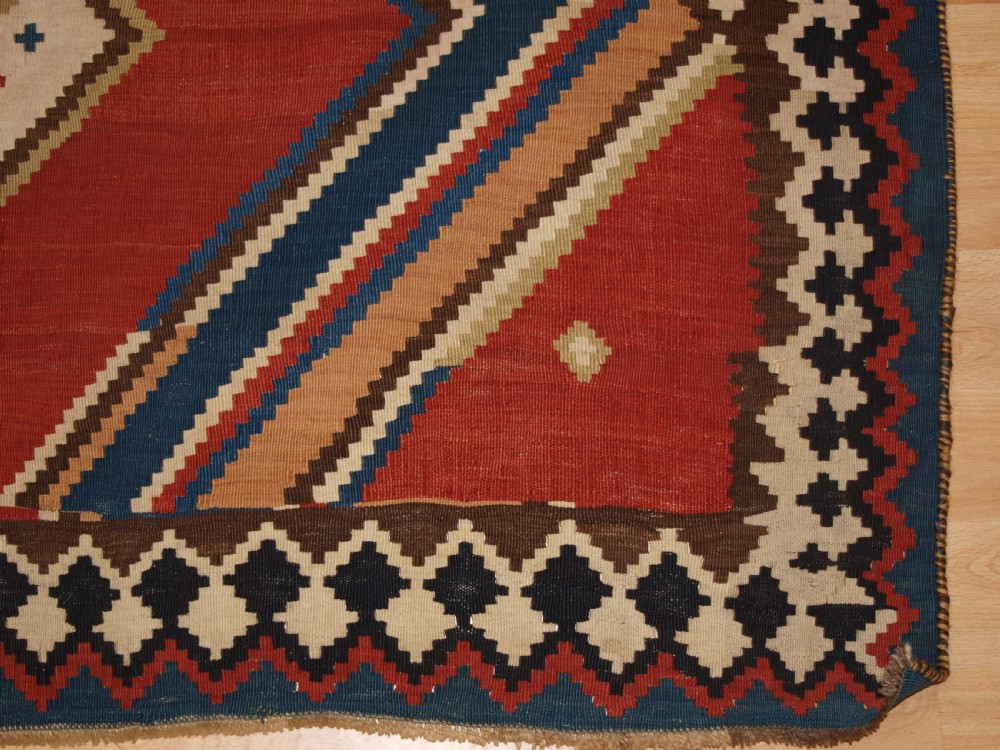 An antique flatweave Qashqai wool kilim rug featuring bold geometric diamond and chevron eye-dazzler patterns in terracotta red, indigo blue, cream, and brown. View XI