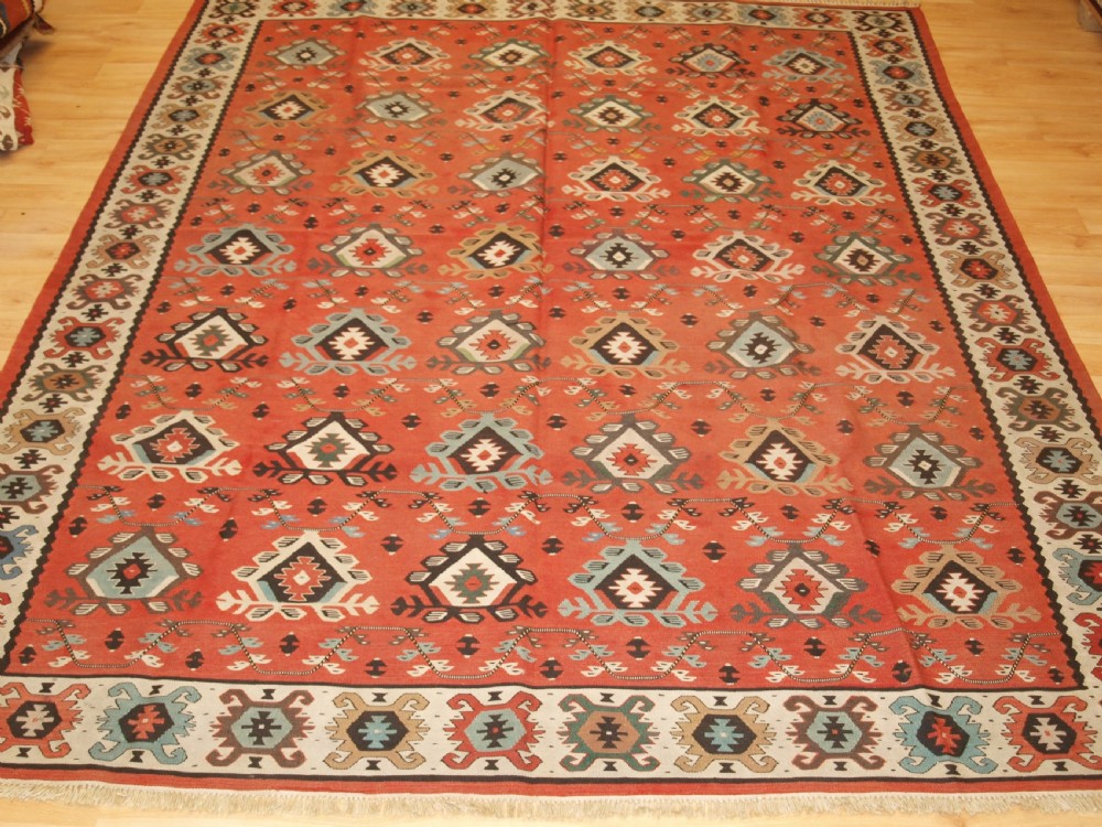 An antique flatwoven wool Sharkoy kilim rug featuring a terracotta red field with repeating geometric diamond motifs in pastel shades and a wide geometric border. View II