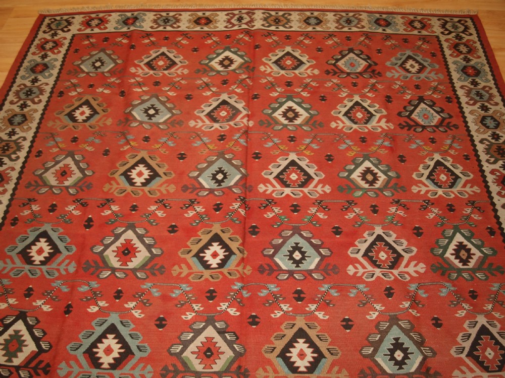 An antique flatwoven wool Sharkoy kilim rug featuring a terracotta red field with repeating geometric diamond motifs in pastel shades and a wide geometric border. View III