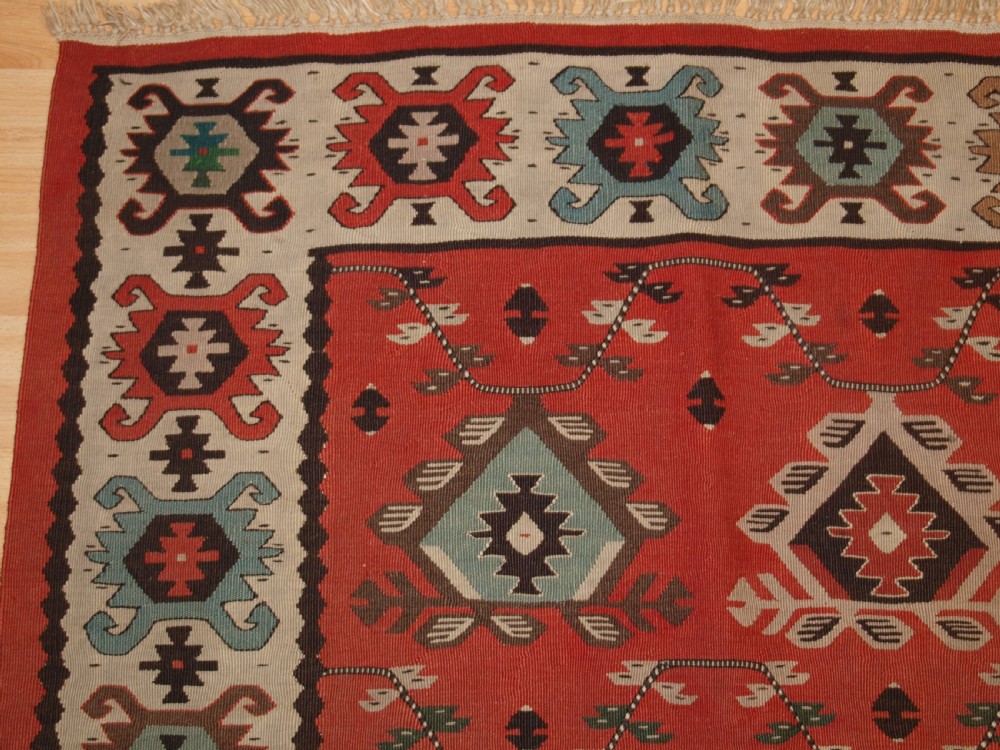 An antique flatwoven wool Sharkoy kilim rug featuring a terracotta red field with repeating geometric diamond motifs in pastel shades and a wide geometric border. View IV