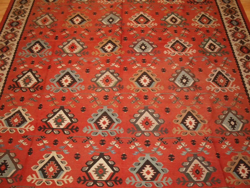 An antique flatwoven wool Sharkoy kilim rug featuring a terracotta red field with repeating geometric diamond motifs in pastel shades and a wide geometric border. View V