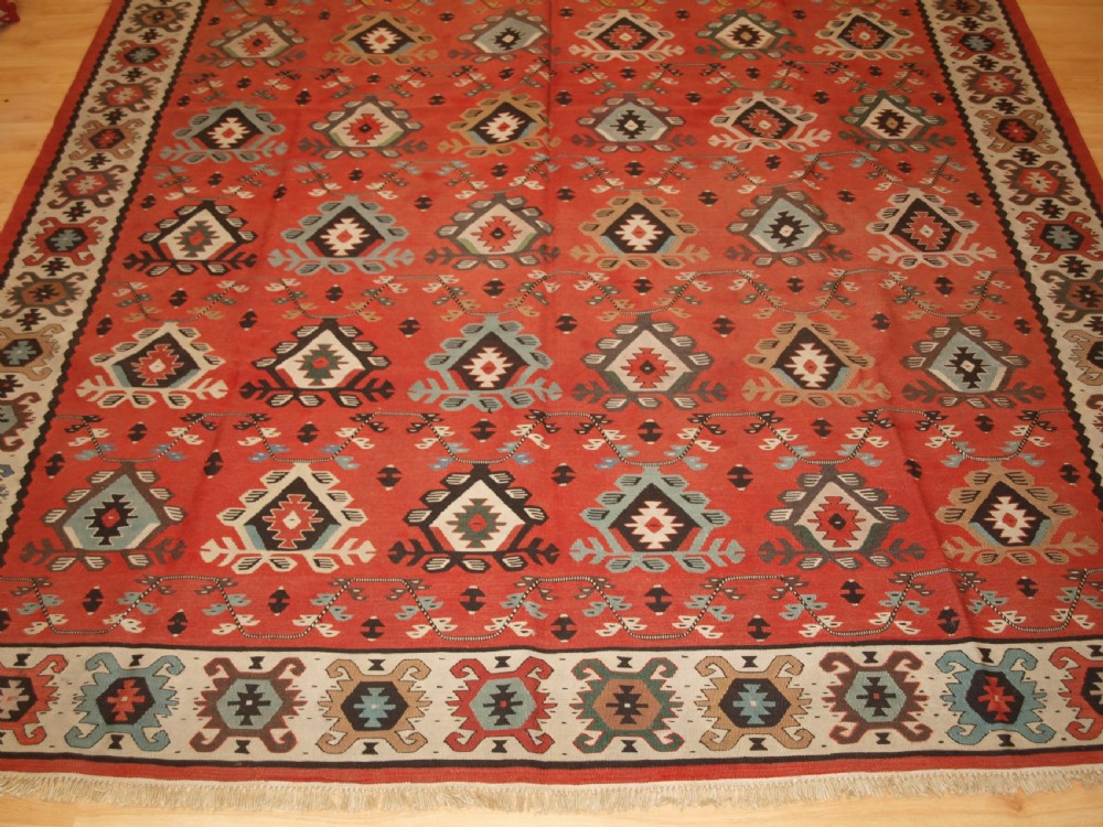 An antique flatwoven wool Sharkoy kilim rug featuring a terracotta red field with repeating geometric diamond motifs in pastel shades and a wide geometric border. View VI