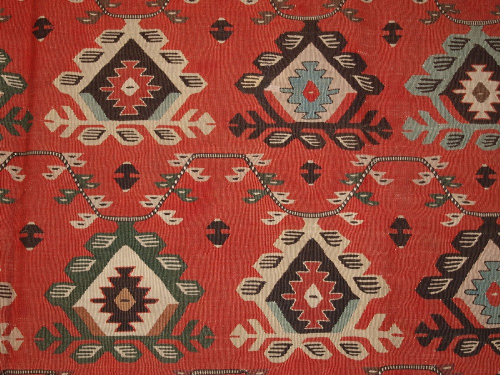 An antique flatwoven wool Sharkoy kilim rug featuring a terracotta red field with repeating geometric diamond motifs in pastel shades and a wide geometric border. View VII