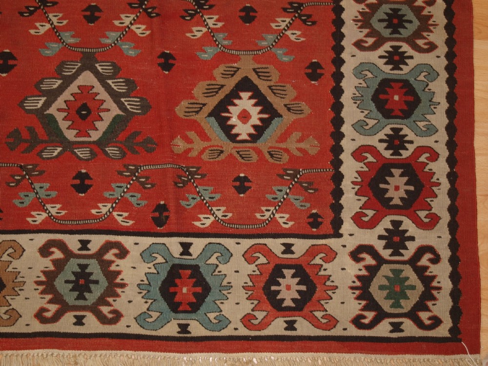 An antique flatwoven wool Sharkoy kilim rug featuring a terracotta red field with repeating geometric diamond motifs in pastel shades and a wide geometric border. View VIII