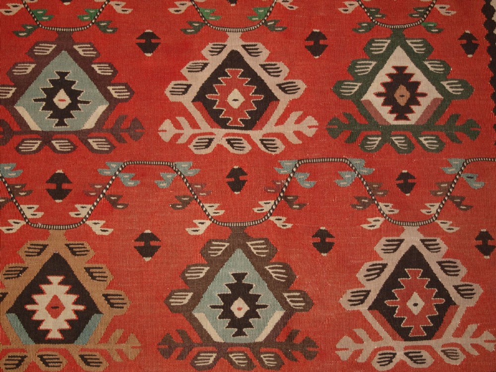 An antique flatwoven wool Sharkoy kilim rug featuring a terracotta red field with repeating geometric diamond motifs in pastel shades and a wide geometric border. View IX