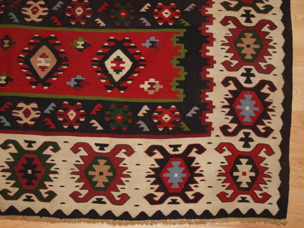 A rectangular handwoven antique wool kilim rug featuring horizontal red and dark brown banded panels decorated with geometric diamond motifs, framed by a broad cream border. View VIII