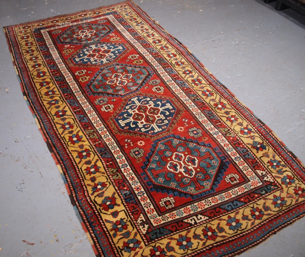 An antique South Caucasian Karabagh long rug featuring five large geometric medallions down a red central field framed by yellow floral and geometric borders.