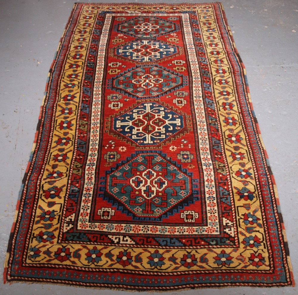 An antique South Caucasian Karabagh long rug featuring five large geometric medallions down a red central field framed by yellow floral and geometric borders. View II