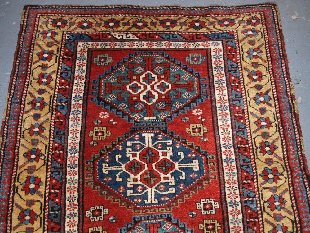 An antique South Caucasian Karabagh long rug featuring five large geometric medallions down a red central field framed by yellow floral and geometric borders. View III
