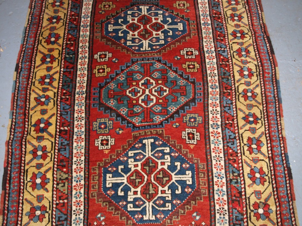 An antique South Caucasian Karabagh long rug featuring five large geometric medallions down a red central field framed by yellow floral and geometric borders. View IV