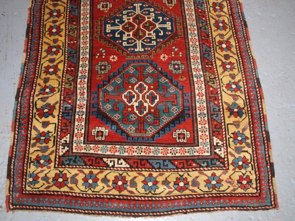 An antique South Caucasian Karabagh long rug featuring five large geometric medallions down a red central field framed by yellow floral and geometric borders. View V