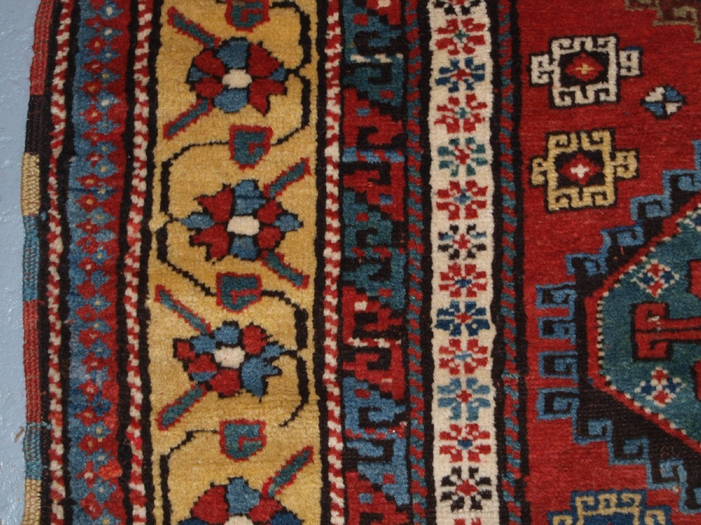 An antique South Caucasian Karabagh long rug featuring five large geometric medallions down a red central field framed by yellow floral and geometric borders. View VII