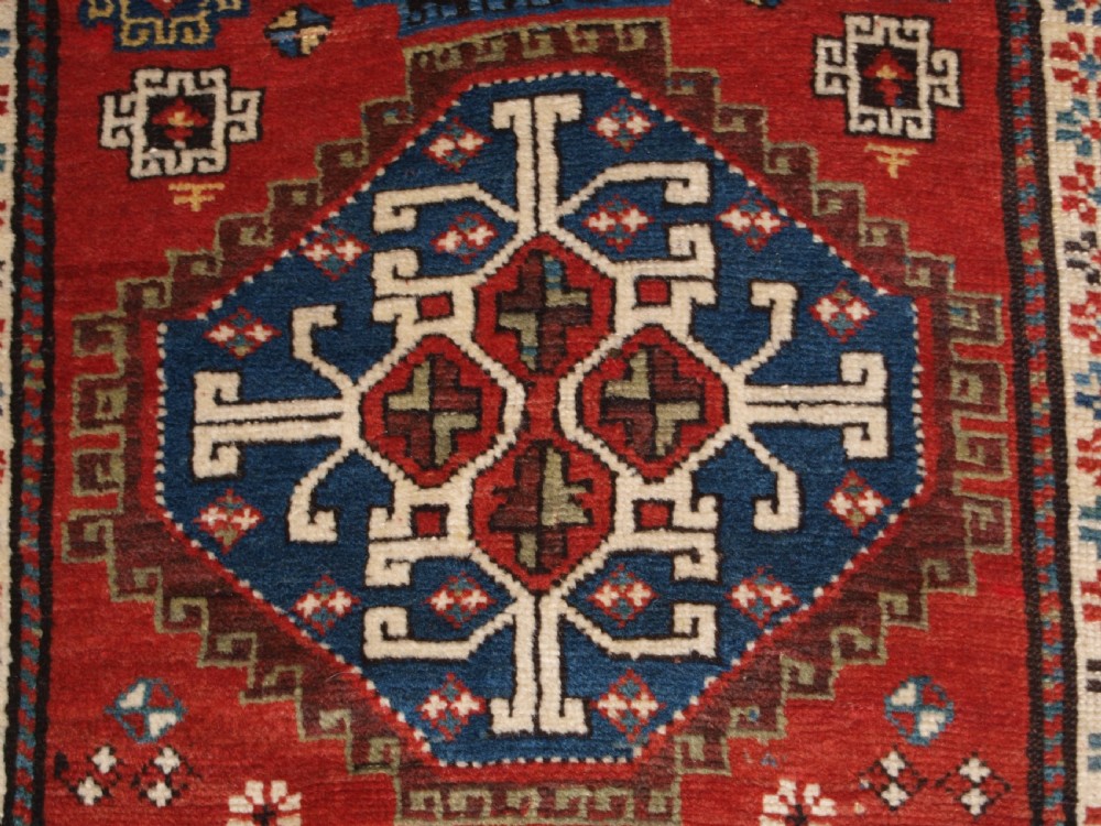 An antique South Caucasian Karabagh long rug featuring five large geometric medallions down a red central field framed by yellow floral and geometric borders. View X