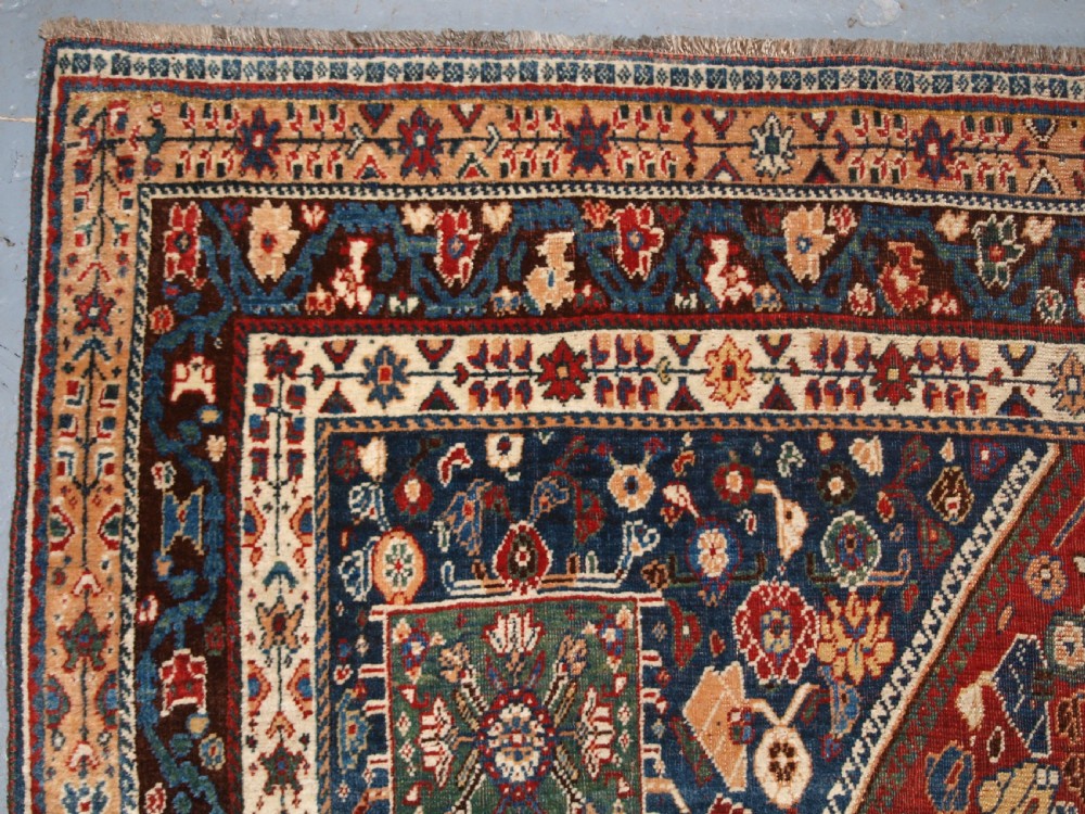 An antique hand-knotted Qashqai Kashkuli wool rug featuring a central red diamond medallion framed by complex floral motifs and multi-band geometric borders. View VI