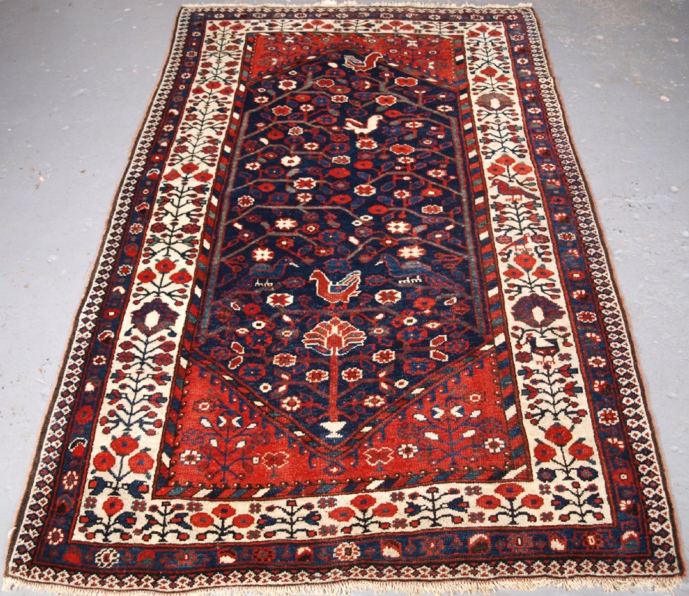 An antique hand-knotted Persian Luri rug featuring a dark navy field filled with stylised bird and floral motifs framed by a red surround and ivory floral border.