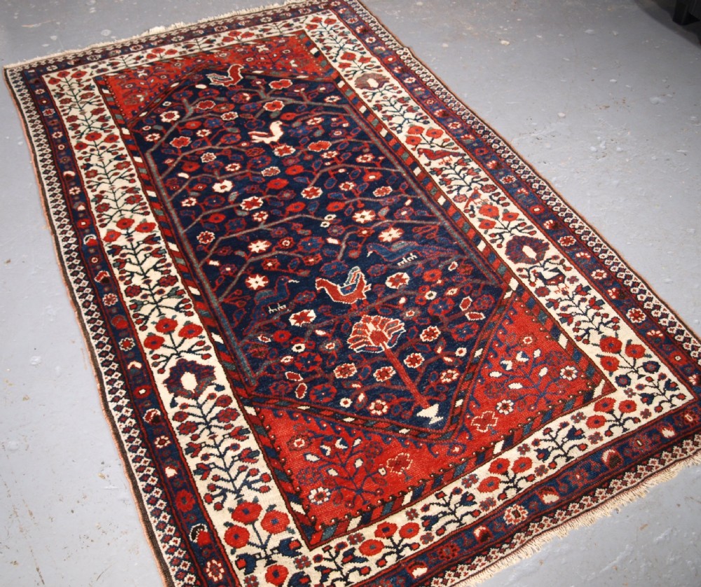 An antique hand-knotted Persian Luri rug featuring a dark navy field filled with stylised bird and floral motifs framed by a red surround and ivory floral border. View II