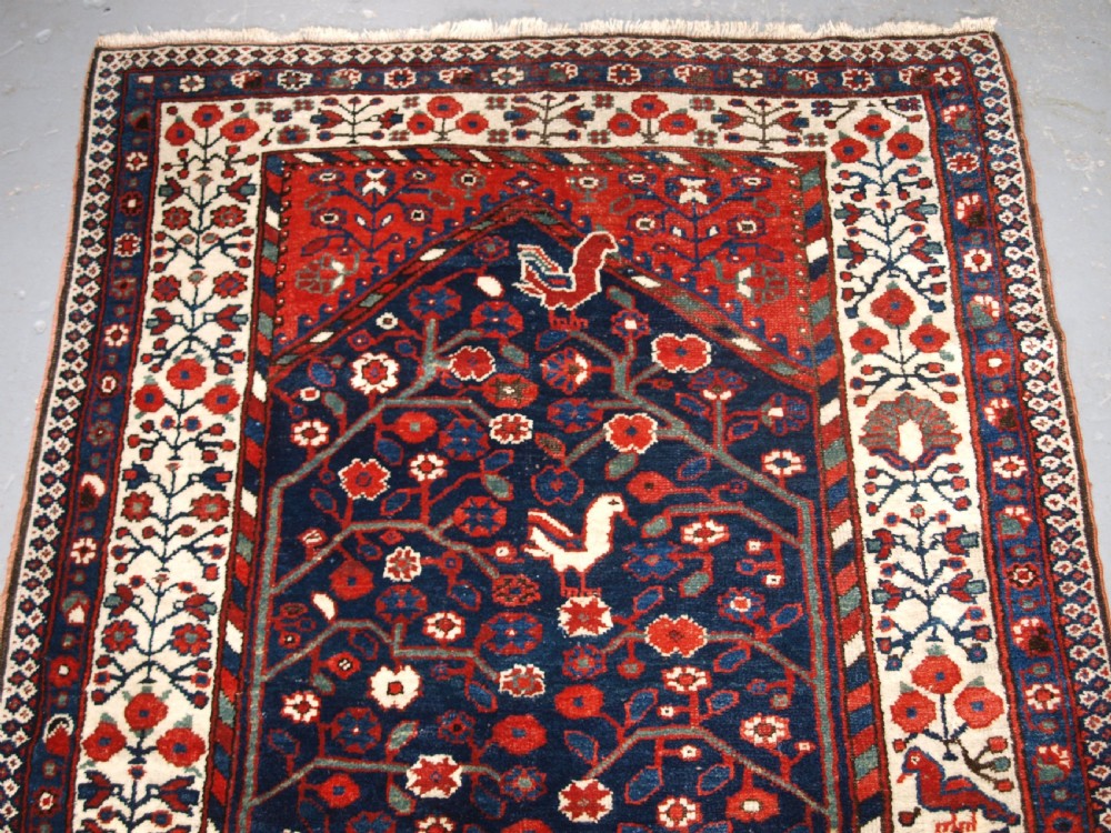 An antique hand-knotted Persian Luri rug featuring a dark navy field filled with stylised bird and floral motifs framed by a red surround and ivory floral border. View III