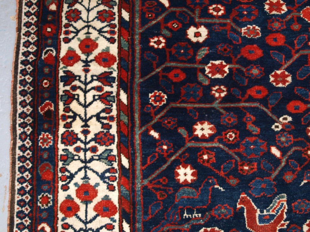 An antique hand-knotted Persian Luri rug featuring a dark navy field filled with stylised bird and floral motifs framed by a red surround and ivory floral border. View VII