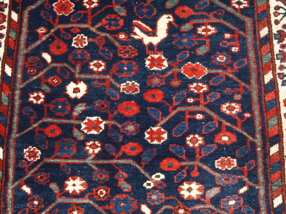 An antique hand-knotted Persian Luri rug featuring a dark navy field filled with stylised bird and floral motifs framed by a red surround and ivory floral border. View X