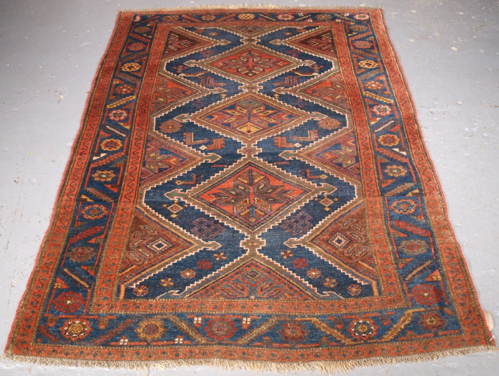An antique hand-knotted wool Kurdish rug featuring three diamond medallion motifs down the centre on a deep blue field with geometric borders.