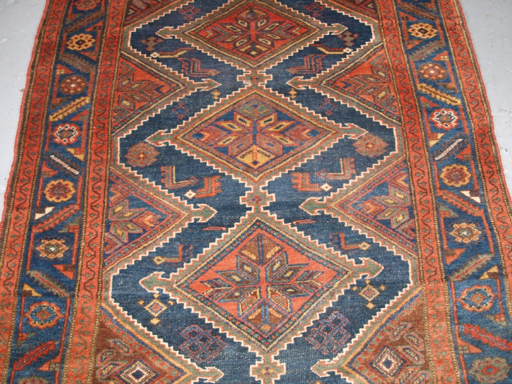 An antique hand-knotted wool Kurdish rug featuring three diamond medallion motifs down the centre on a deep blue field with geometric borders. View III