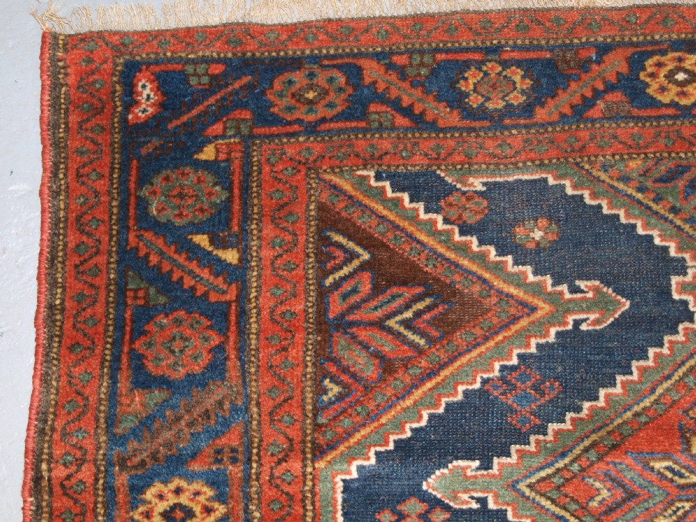 An antique hand-knotted wool Kurdish rug featuring three diamond medallion motifs down the centre on a deep blue field with geometric borders. View V