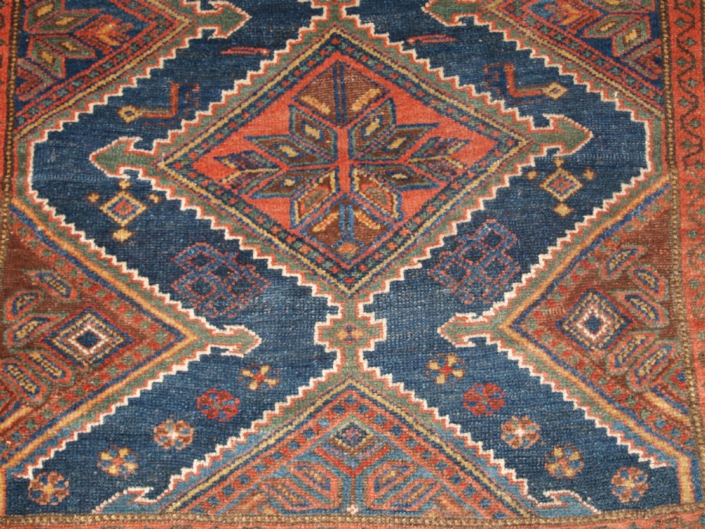 An antique hand-knotted wool Kurdish rug featuring three diamond medallion motifs down the centre on a deep blue field with geometric borders. View X