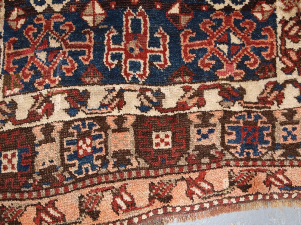 An antique Turkish Bergama rug featuring hand-knotted geometric motifs in shades of terracotta red, navy blue, and cream. View X