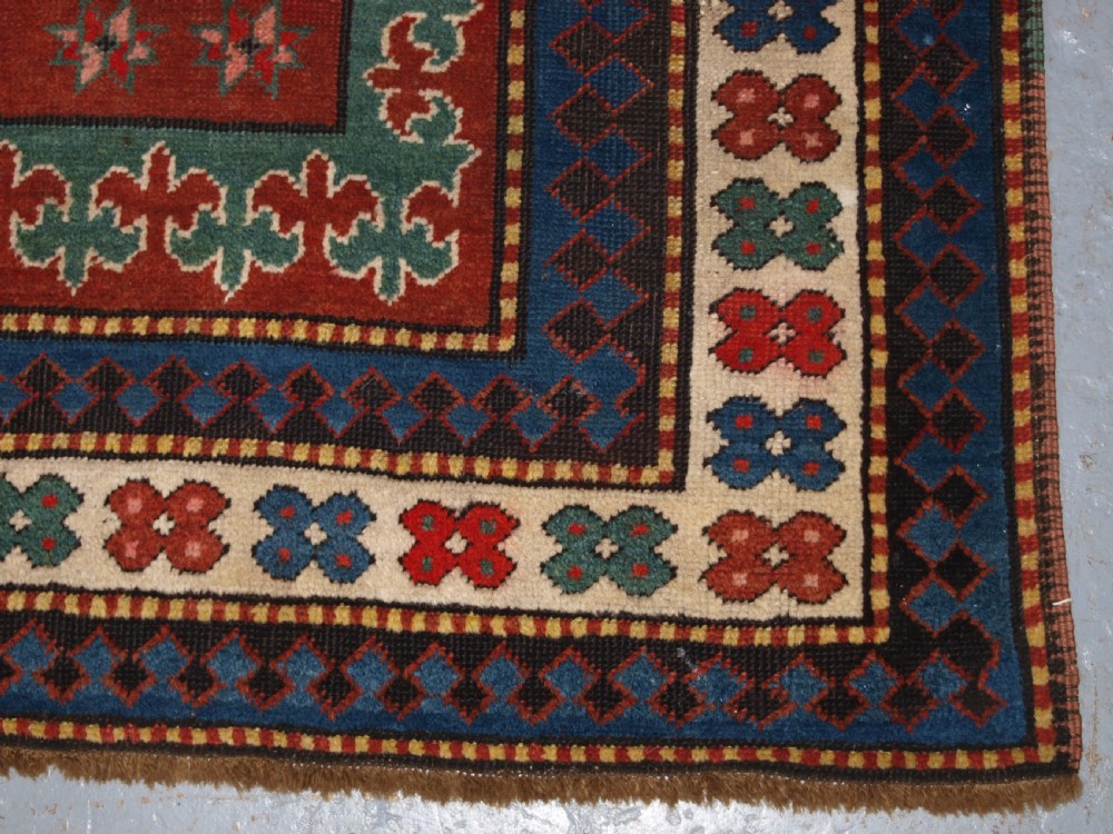 An antique Caucasian rug featuring a red field woven with five stacked geometric medallions, small animal figures, and multi-coloured patterned borders. View XVI