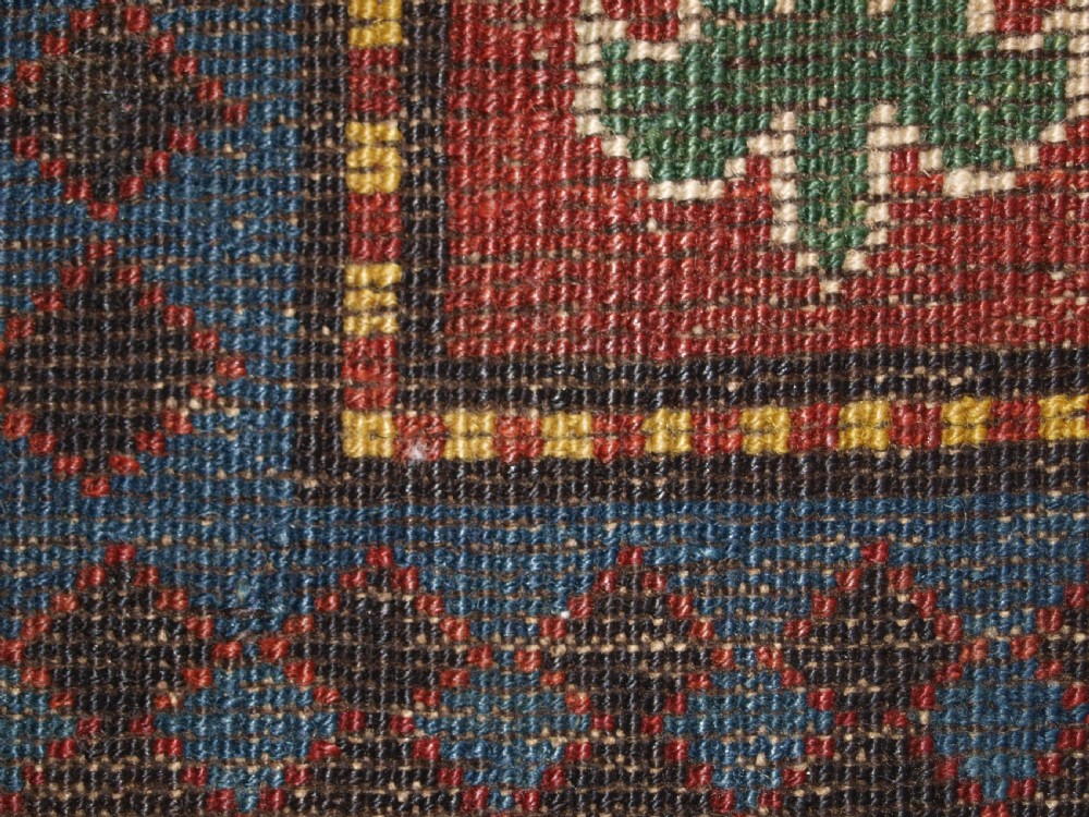 An antique Caucasian rug featuring a red field woven with five stacked geometric medallions, small animal figures, and multi-coloured patterned borders. View XVII