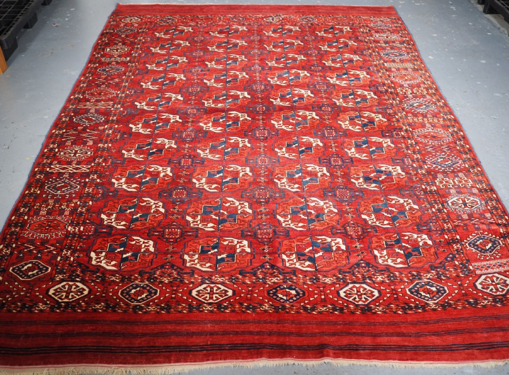 A large hand-knotted antique Tekke Turkmen main carpet in deep red featuring a four by ten grid of octagonal gul motifs framed by detailed geometric borders.
