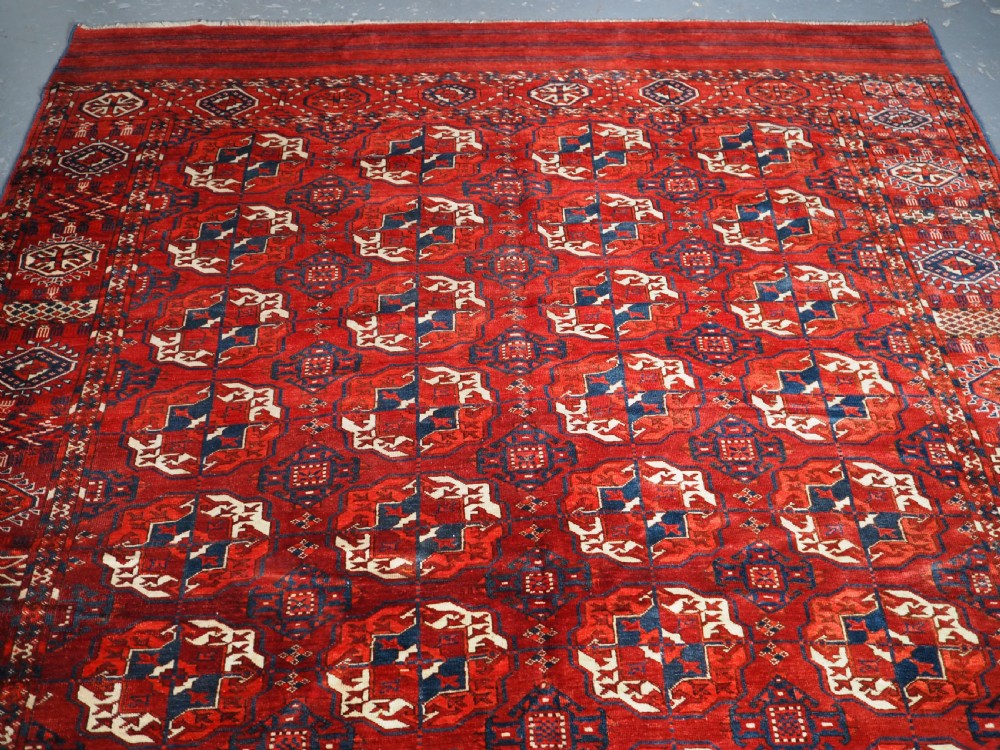 A large hand-knotted antique Tekke Turkmen main carpet in deep red featuring a four by ten grid of octagonal gul motifs framed by detailed geometric borders. View II