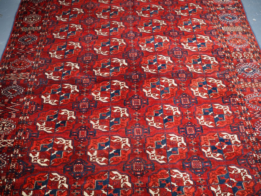 A large hand-knotted antique Tekke Turkmen main carpet in deep red featuring a four by ten grid of octagonal gul motifs framed by detailed geometric borders. View III