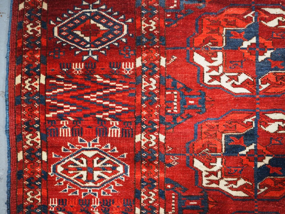 A large hand-knotted antique Tekke Turkmen main carpet in deep red featuring a four by ten grid of octagonal gul motifs framed by detailed geometric borders. View IV