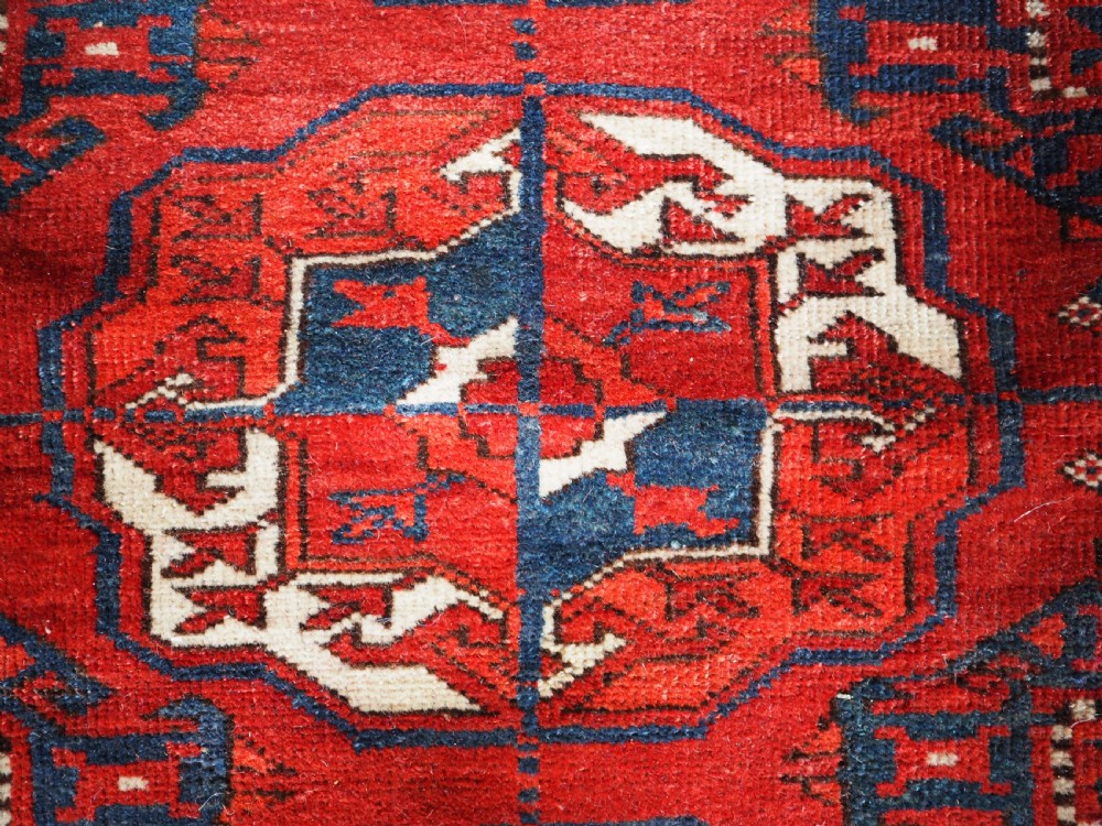 A large hand-knotted antique Tekke Turkmen main carpet in deep red featuring a four by ten grid of octagonal gul motifs framed by detailed geometric borders. View VI