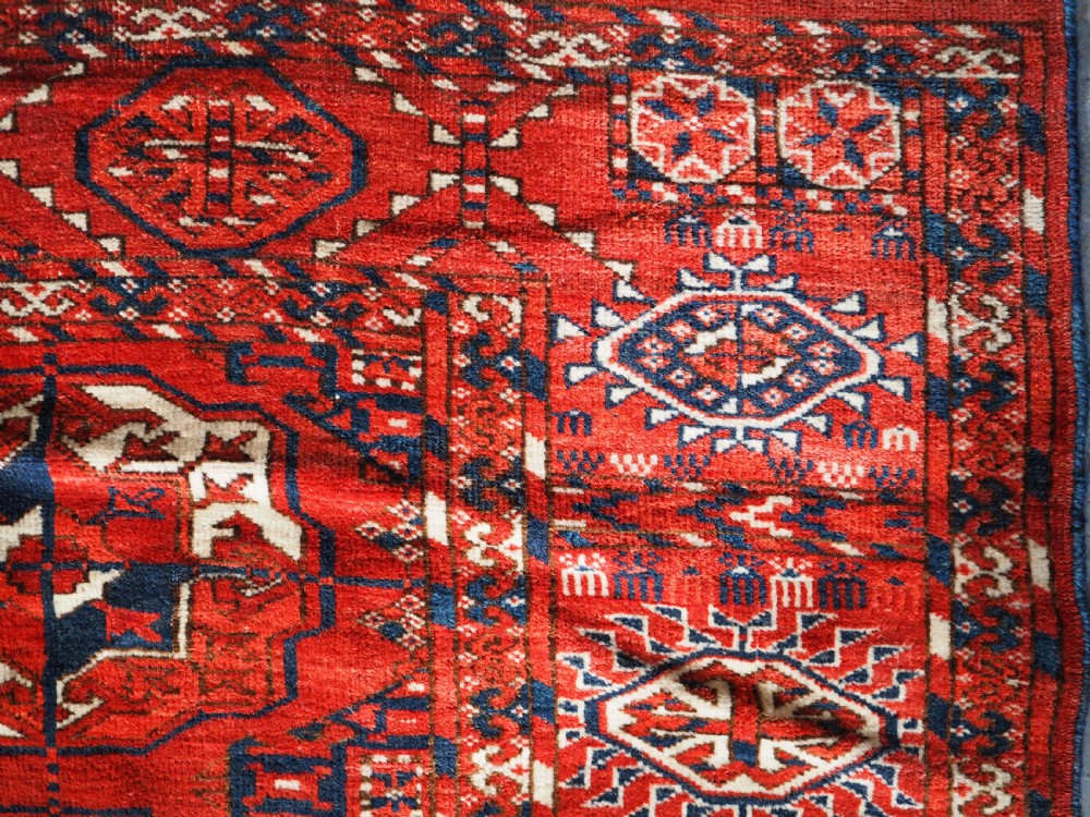 A large hand-knotted antique Tekke Turkmen main carpet in deep red featuring a four by ten grid of octagonal gul motifs framed by detailed geometric borders. View IX